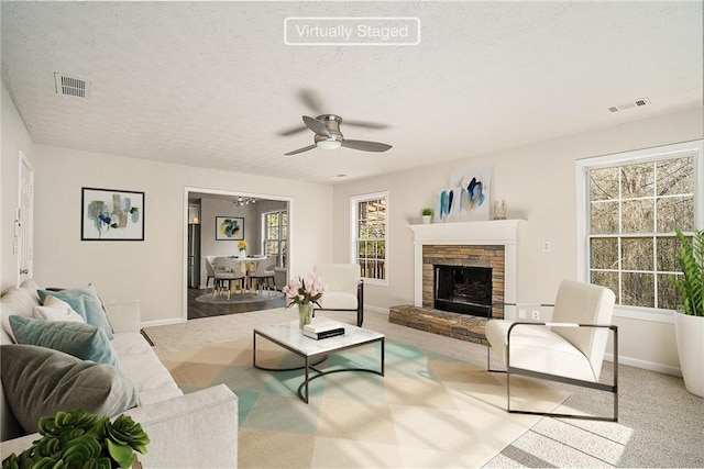 carpeted living room featuring ceiling fan, a fireplace, and a textured ceiling