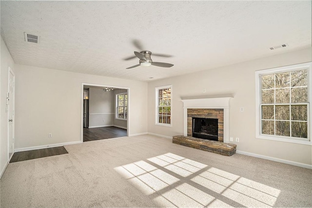 unfurnished living room featuring a stone fireplace, ceiling fan, dark carpet, and a textured ceiling