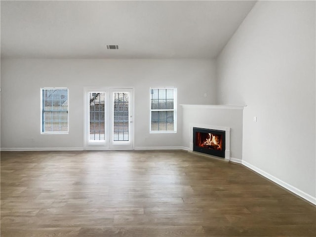 unfurnished living room featuring a warm lit fireplace, baseboards, visible vents, and dark wood finished floors
