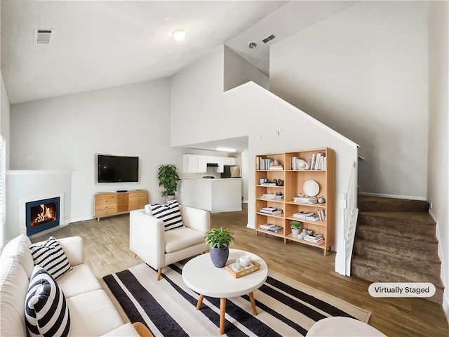 living room with a warm lit fireplace, high vaulted ceiling, visible vents, stairway, and light wood-type flooring