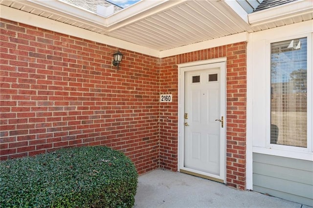 doorway to property featuring brick siding and roof with shingles