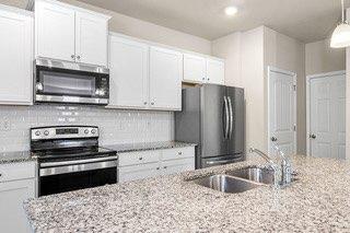 kitchen with light stone counters, a sink, white cabinetry, and appliances with stainless steel finishes