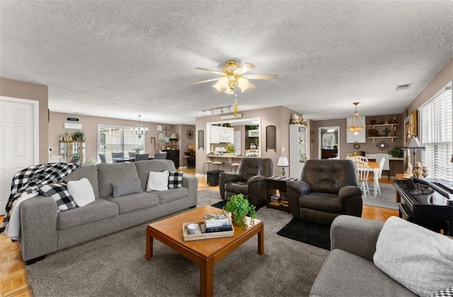 living room with ceiling fan with notable chandelier, a textured ceiling, and light parquet floors