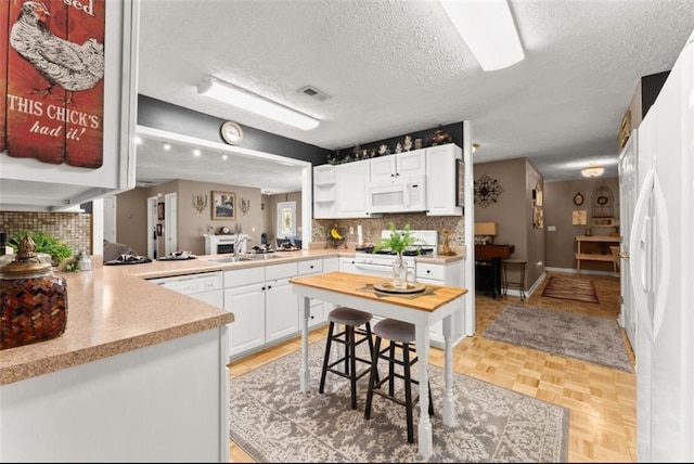 kitchen with white appliances, kitchen peninsula, a textured ceiling, light parquet floors, and white cabinets