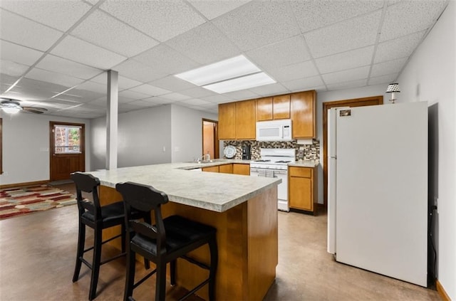 kitchen with white appliances, a paneled ceiling, a breakfast bar, decorative backsplash, and ceiling fan