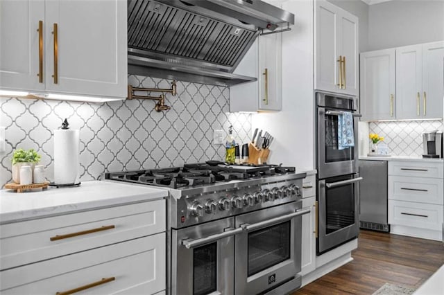 kitchen with appliances with stainless steel finishes, white cabinetry, dark hardwood / wood-style floors, light stone countertops, and custom exhaust hood