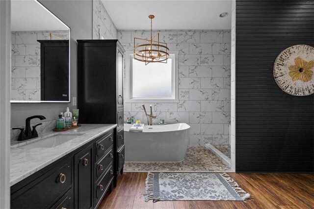 bathroom featuring tile walls, a tub to relax in, hardwood / wood-style flooring, vanity, and a notable chandelier