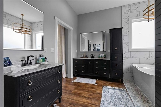 bathroom featuring hardwood / wood-style flooring, vanity, a notable chandelier, and a tub to relax in