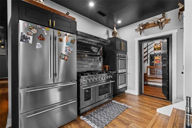 kitchen featuring tasteful backsplash, high quality appliances, extractor fan, and light wood-type flooring