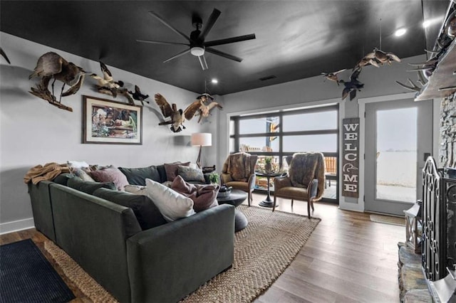 living room with hardwood / wood-style floors, a stone fireplace, and ceiling fan