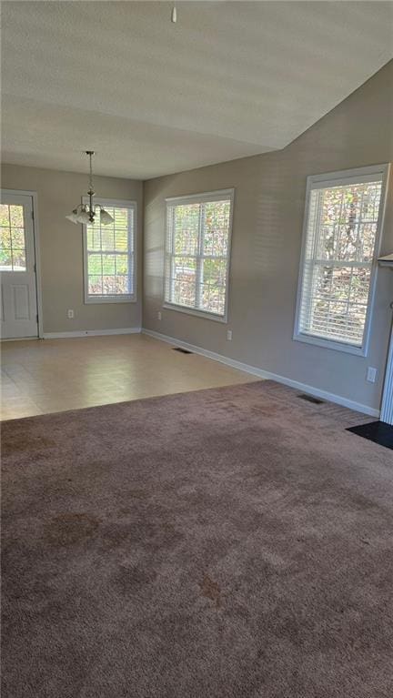 empty room featuring carpet flooring, a textured ceiling, a chandelier, and vaulted ceiling