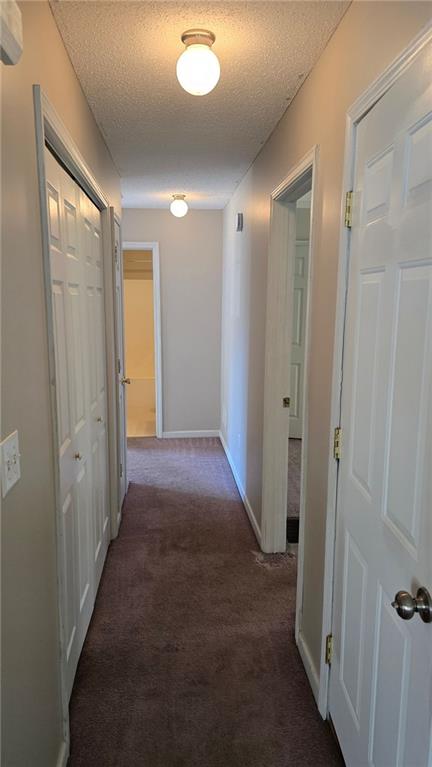 hall featuring a textured ceiling and dark colored carpet