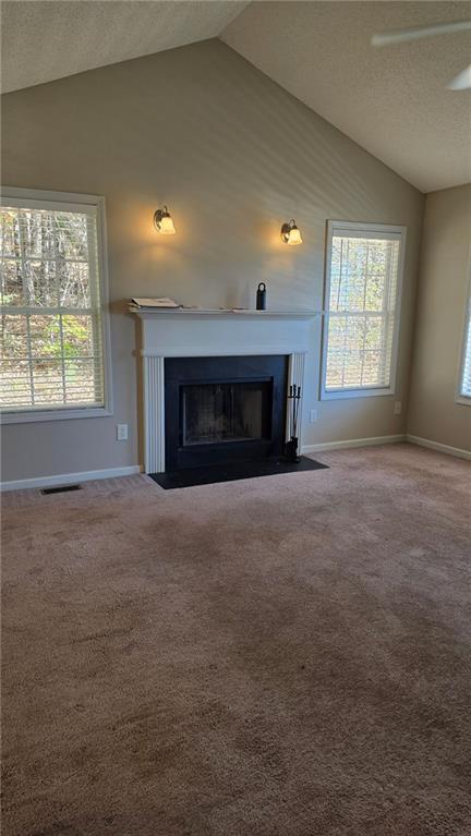 unfurnished living room with a textured ceiling, carpet floors, vaulted ceiling, and ceiling fan