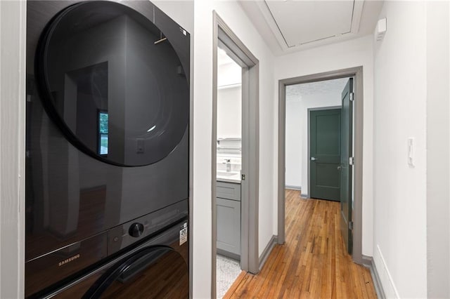 washroom with stacked washer / dryer, a sink, light wood-style floors, baseboards, and laundry area