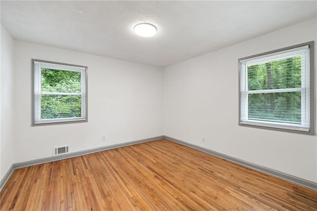 unfurnished room with a wealth of natural light, visible vents, light wood-style flooring, and baseboards