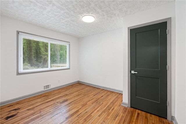 spare room with a textured ceiling, visible vents, light wood-style flooring, and baseboards