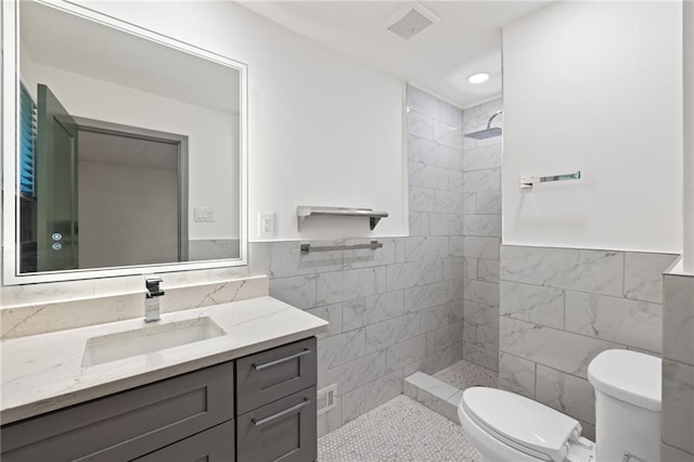 full bathroom featuring a tile shower, tile walls, toilet, vanity, and visible vents