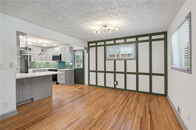 kitchen with light wood-style flooring, appliances with stainless steel finishes, decorative backsplash, and light countertops