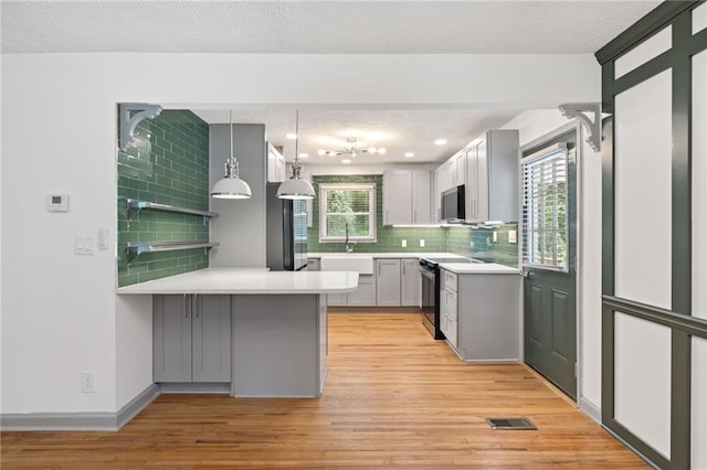 kitchen with a peninsula, black / electric stove, light wood-style flooring, and backsplash