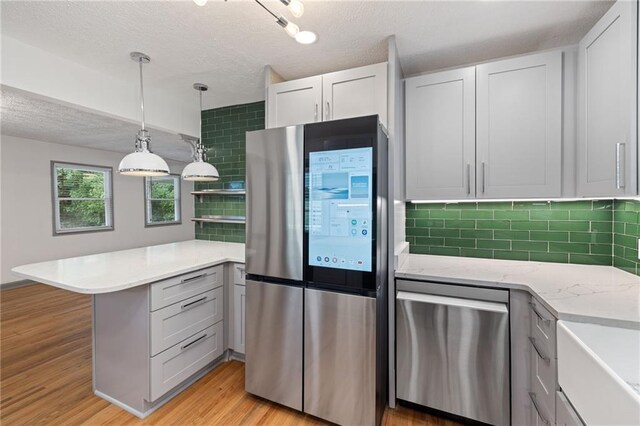 kitchen featuring a textured ceiling, tasteful backsplash, light wood-style flooring, appliances with stainless steel finishes, and a peninsula