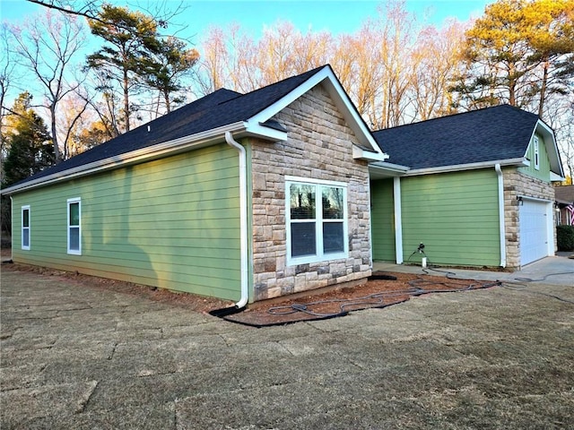 view of side of property with stone siding, a shingled roof, and an attached garage