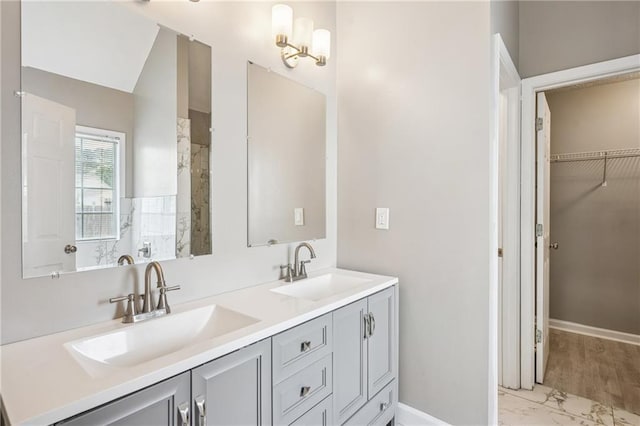 bathroom with marble finish floor, a sink, double vanity, and a spacious closet