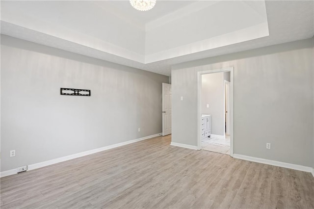 empty room with baseboards, light wood-style floors, and a tray ceiling