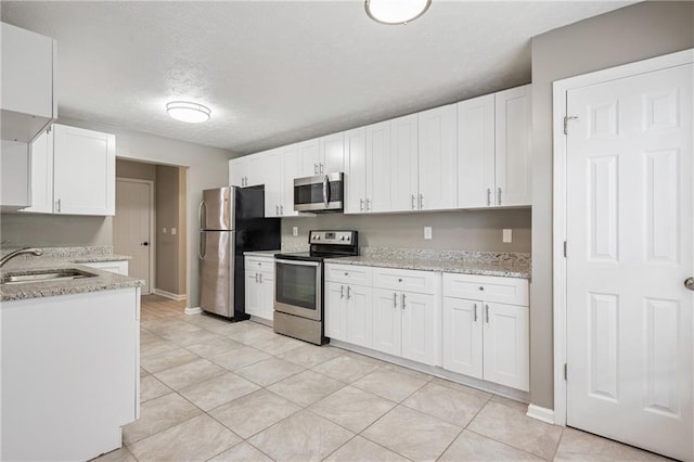kitchen featuring a sink, light stone counters, baseboards, white cabinets, and appliances with stainless steel finishes