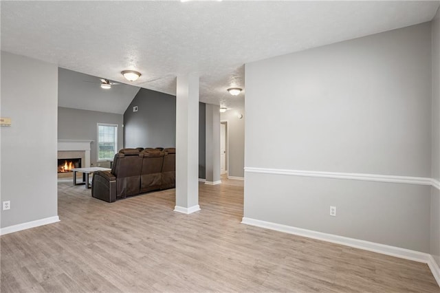 living room with a warm lit fireplace, light wood-style flooring, baseboards, a textured ceiling, and lofted ceiling