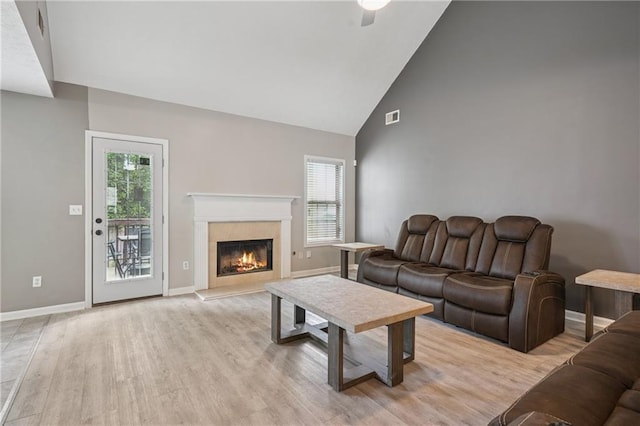living room featuring a fireplace, high vaulted ceiling, visible vents, light wood-style flooring, and baseboards