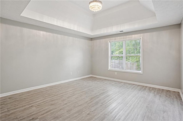 spare room featuring baseboards, visible vents, wood finished floors, and a tray ceiling