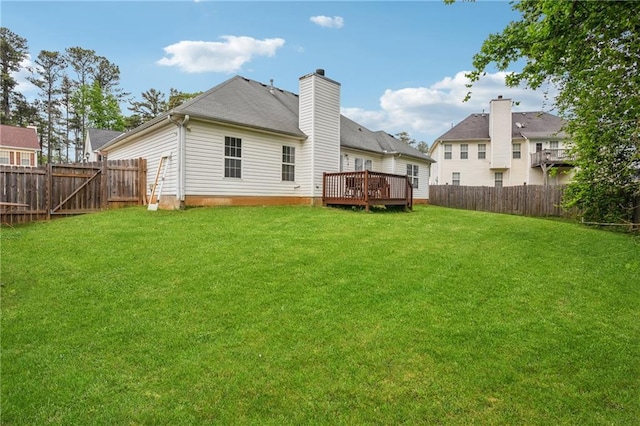 rear view of property with a lawn, a deck, a chimney, and a fenced backyard