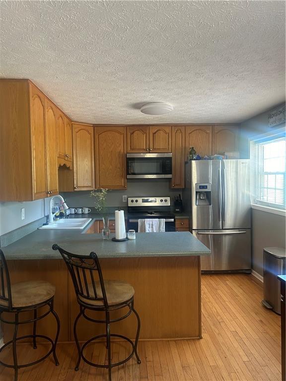 kitchen featuring kitchen peninsula, appliances with stainless steel finishes, light wood-type flooring, and sink