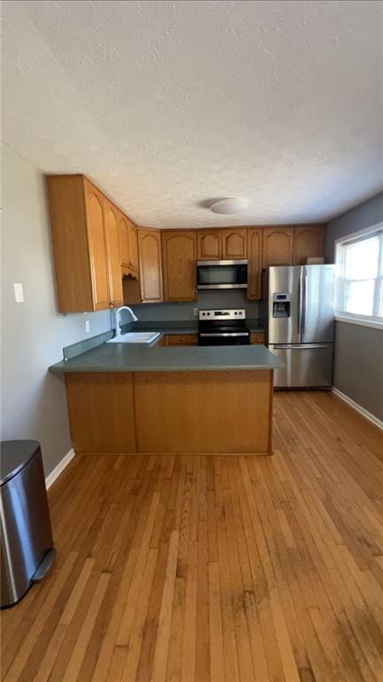 kitchen featuring kitchen peninsula, light wood-type flooring, a textured ceiling, stainless steel appliances, and sink