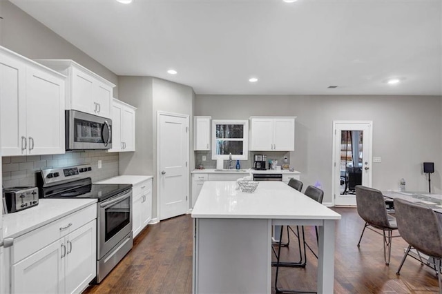 kitchen with a breakfast bar area, dark hardwood / wood-style flooring, a kitchen island, stainless steel appliances, and white cabinets