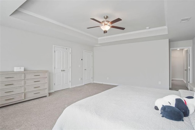 bedroom with ceiling fan, a tray ceiling, ornamental molding, light carpet, and multiple closets