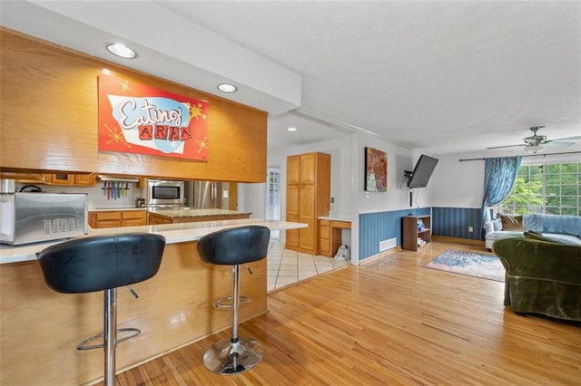 1690 Cedar Grove Dr, Marietta, GA 30066 - kitchen featuring light countertops, light wood-style flooring, a wainscoted wall, a breakfast bar, and a ceiling fan