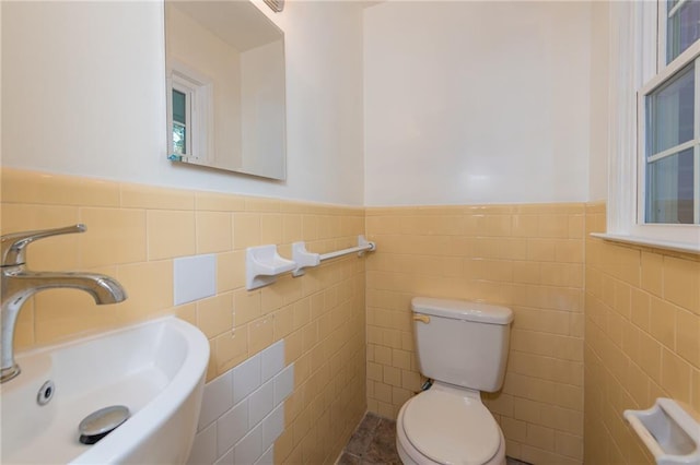 bathroom with wainscoting, a sink, toilet, and tile walls