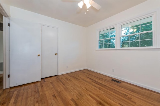 unfurnished room with a ceiling fan, visible vents, baseboards, and wood finished floors