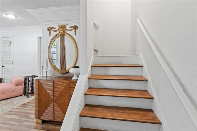 stairway featuring wood finished floors, a textured ceiling, and ornamental molding