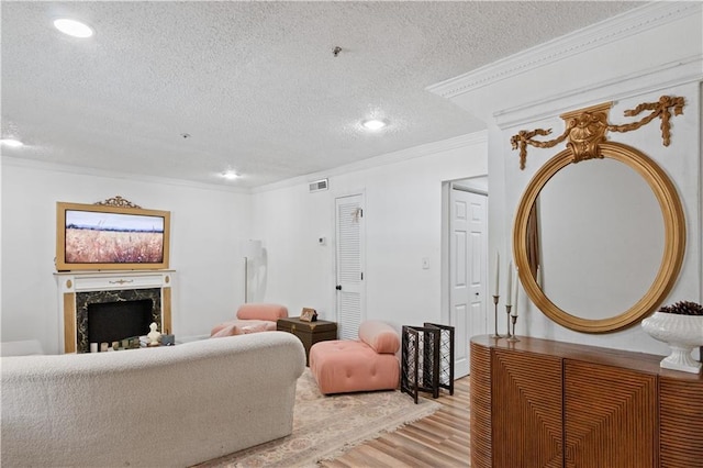 living area featuring light wood-style flooring, crown molding, a textured ceiling, a fireplace, and recessed lighting