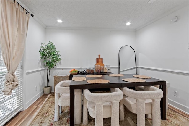 dining space featuring light wood-style floors, a textured ceiling, ornamental molding, recessed lighting, and baseboards