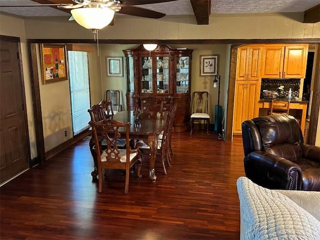 dining room featuring baseboards, dark wood-style floors, beam ceiling, and ceiling fan