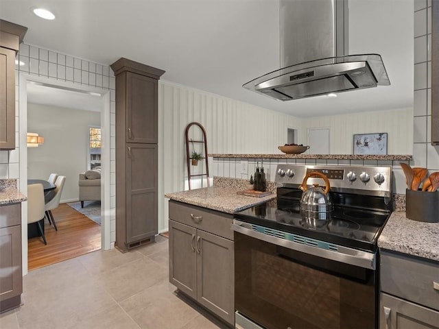 kitchen with island exhaust hood, light tile patterned floors, light stone countertops, and stainless steel range with electric stovetop