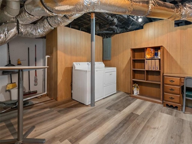 laundry room with washer and clothes dryer, wood walls, wood-type flooring, and electric panel