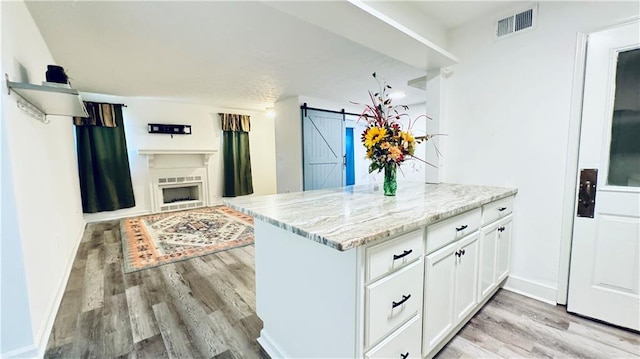 kitchen with visible vents, white cabinets, a barn door, light wood-type flooring, and light stone countertops