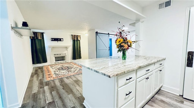 kitchen featuring visible vents, a barn door, light wood-type flooring, white cabinetry, and light stone countertops