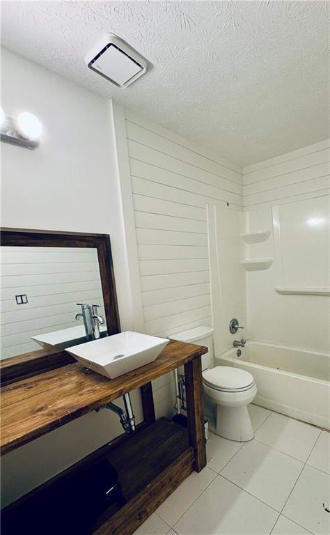 full bathroom with tile patterned flooring,  shower combination, a textured ceiling, and toilet