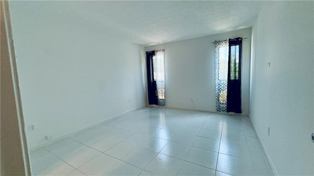 unfurnished room with a textured ceiling, light tile patterned floors, and baseboards