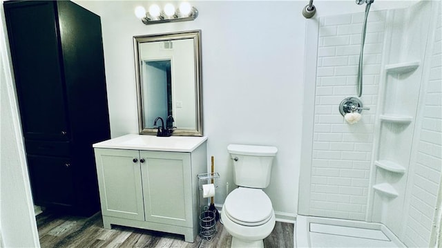 bathroom with vanity, baseboards, toilet, tiled shower, and wood finished floors